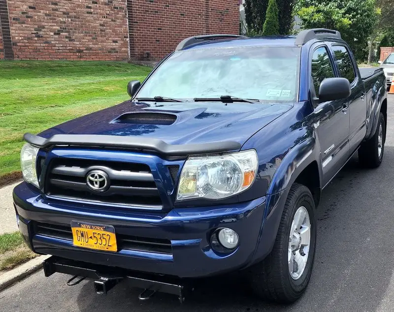 Blue Toyota Tacoma pickup with a hood scoop parked at the curb after repair